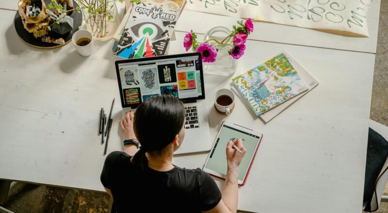 Artistic workspace featuring calligraphy and digital design on a tablet and laptop.