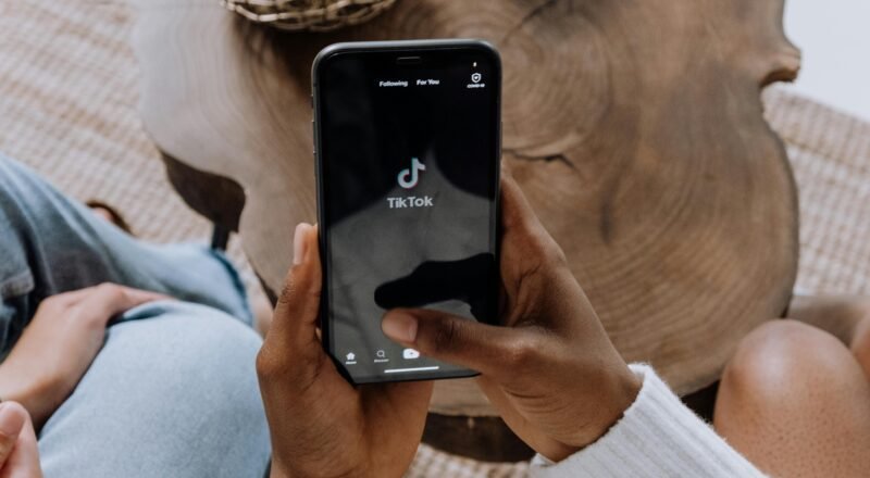 Close-up of hands holding a smartphone displaying the TikTok app interface on a wooden surface.